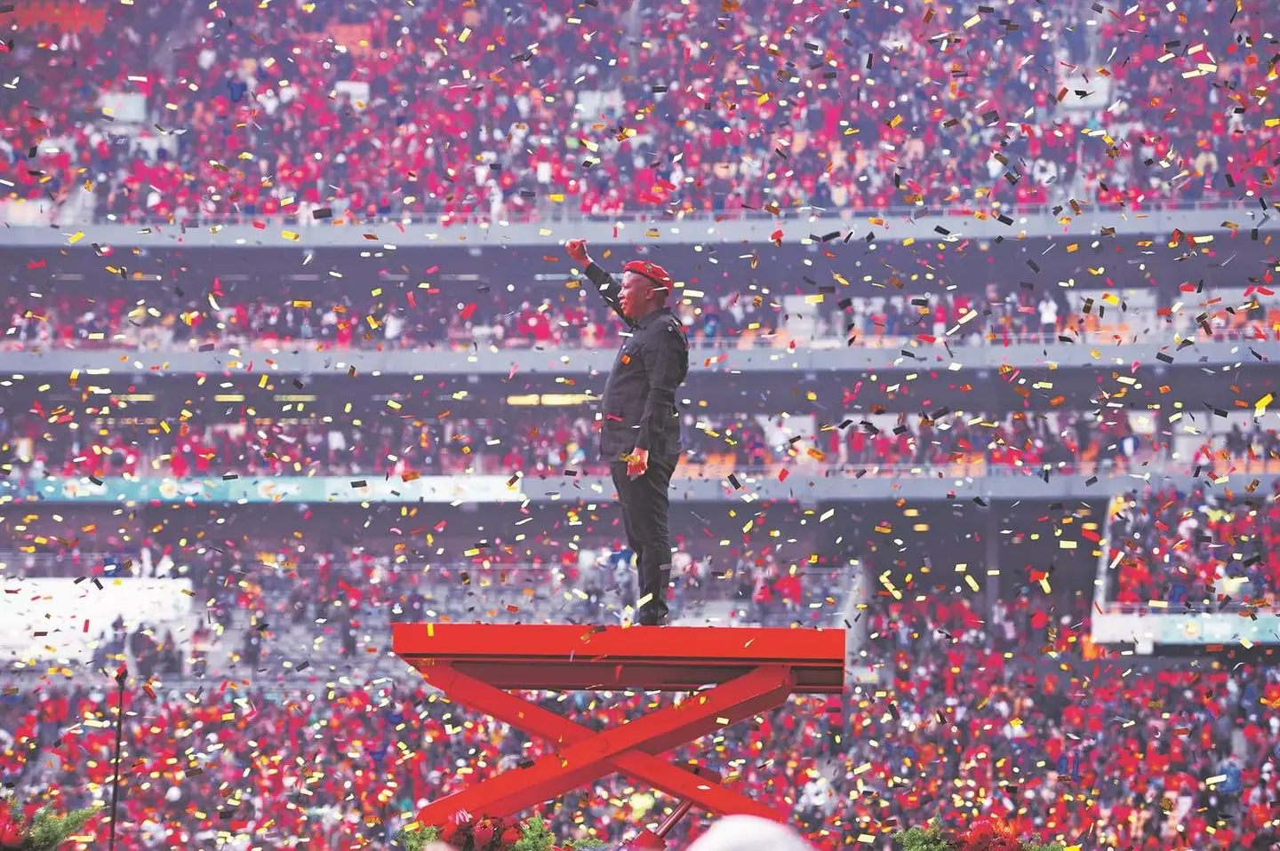 Julius Malema standing on a platform in a stadium packed with EFF supporters